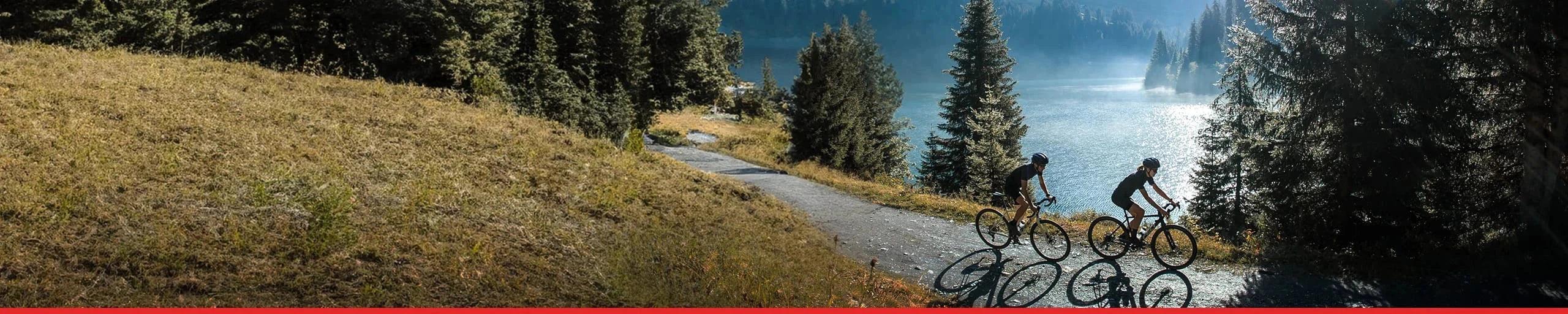 un homme et une femme faisant du vélo de gravel au bord d'un lac, équipés de pneus VITTORIA